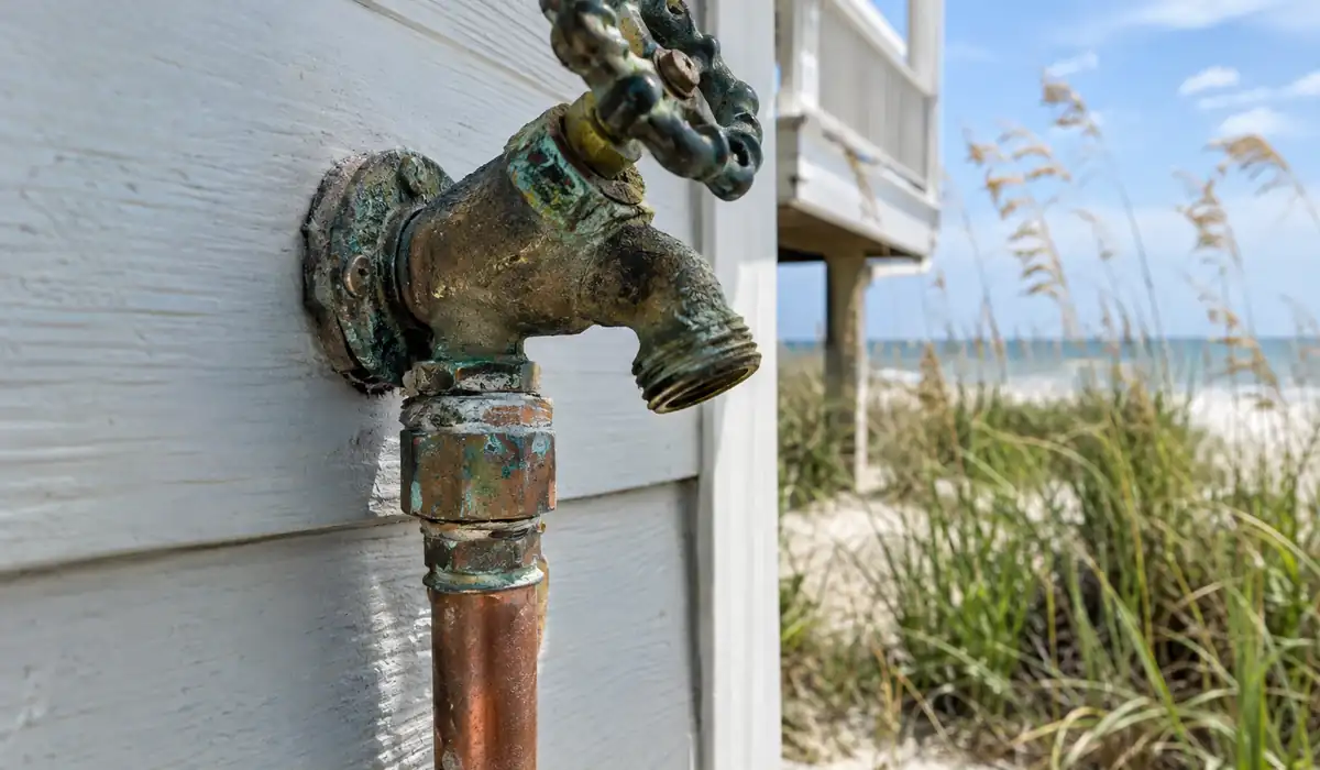 Corroded outdoor hose bib and copper fitting on a stucco wall near the beach